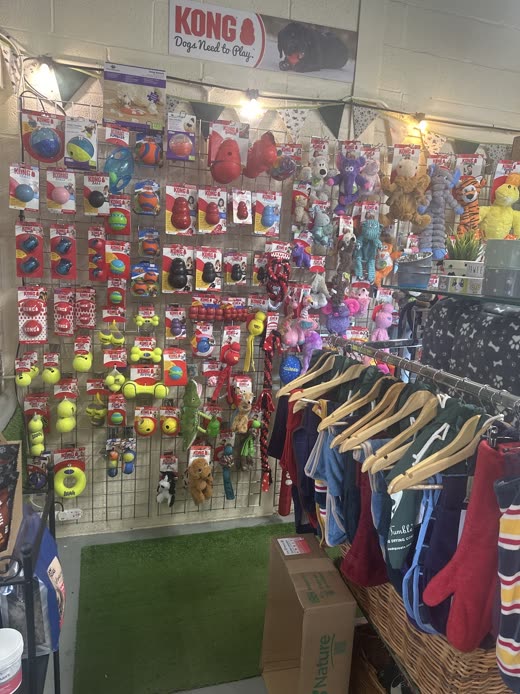 Wall of hanging dog toys and balls beside a rail of dog coats